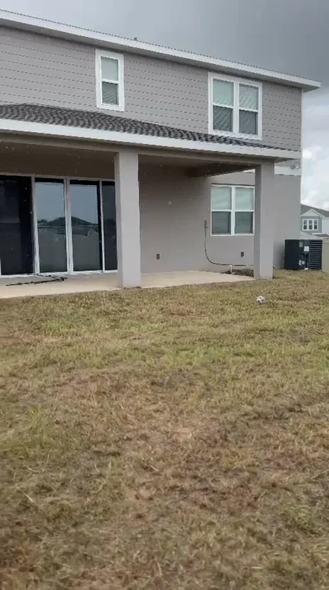 The same backyard after mowing, with the grass cut short around the covered patio.