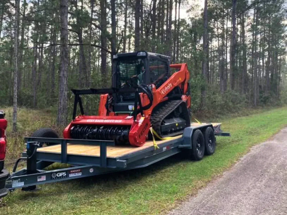 Orange compact track loader secured on a flatbed trailer