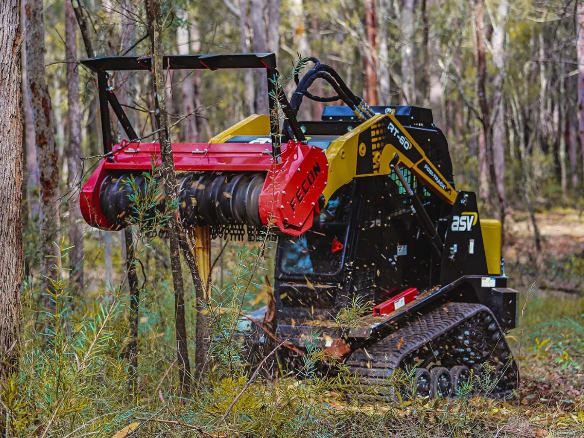 Tracked loader using a Fecon mulcher to clear vegetation among trees.