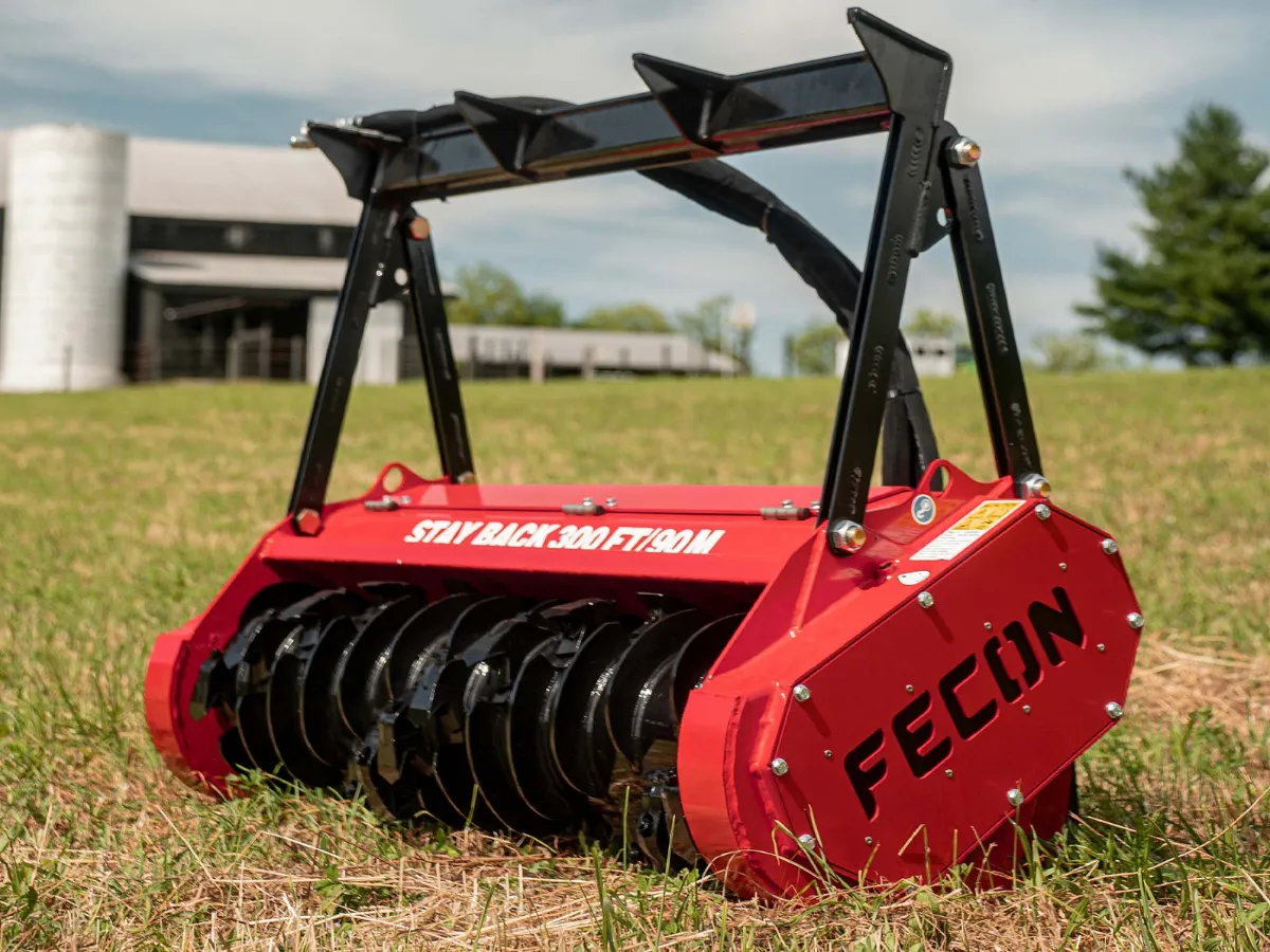 Red Fecon mulcher attachment with black rotor and push bar on grass.