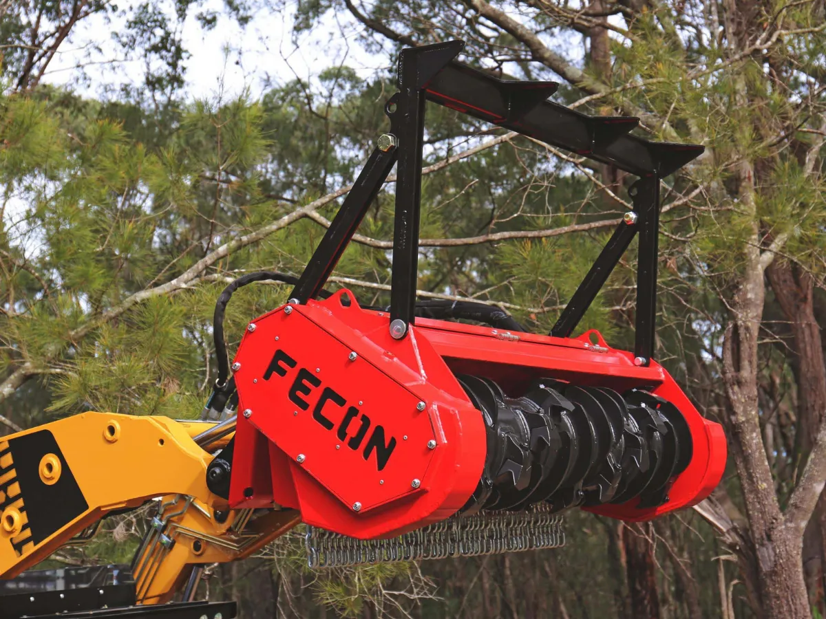 Fecon mulcher raised on a loader with the rotor and chain curtain visible.