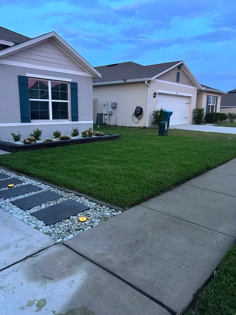 The same front yard after landscaping, with new plants, decorative stone, and a defined bed border.
