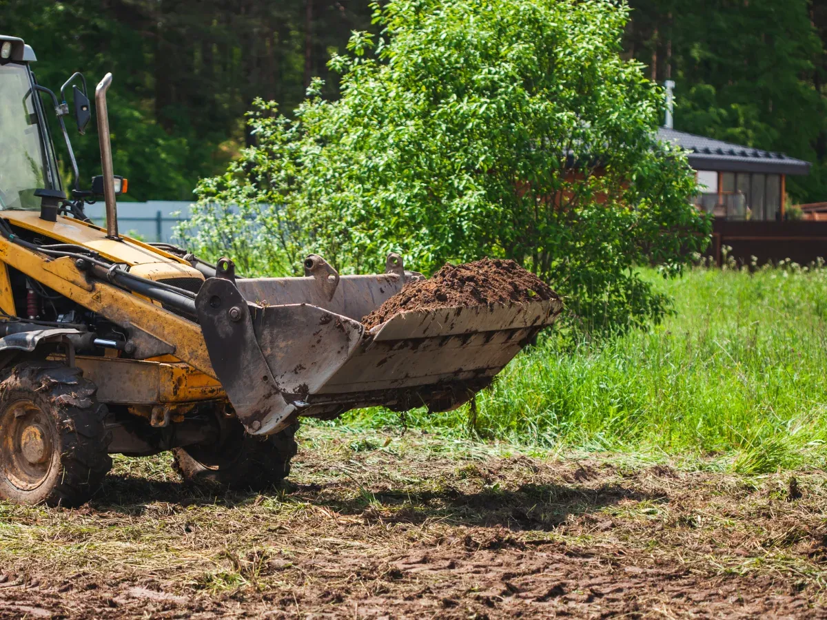 Front loader carrying soil on a partially cleared grassy lot