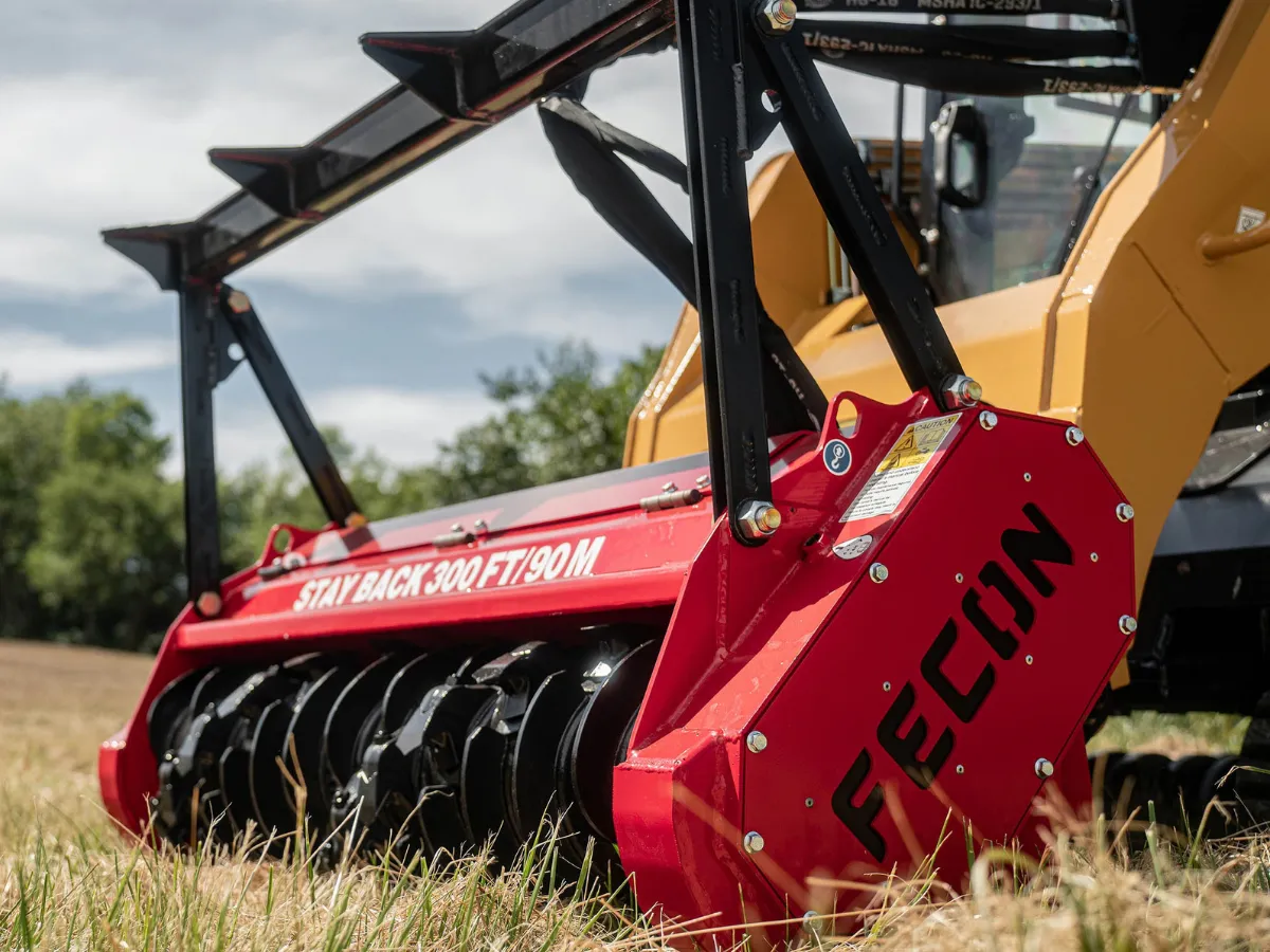 Red Fecon mulcher mounted on a loader with its push bar visible.